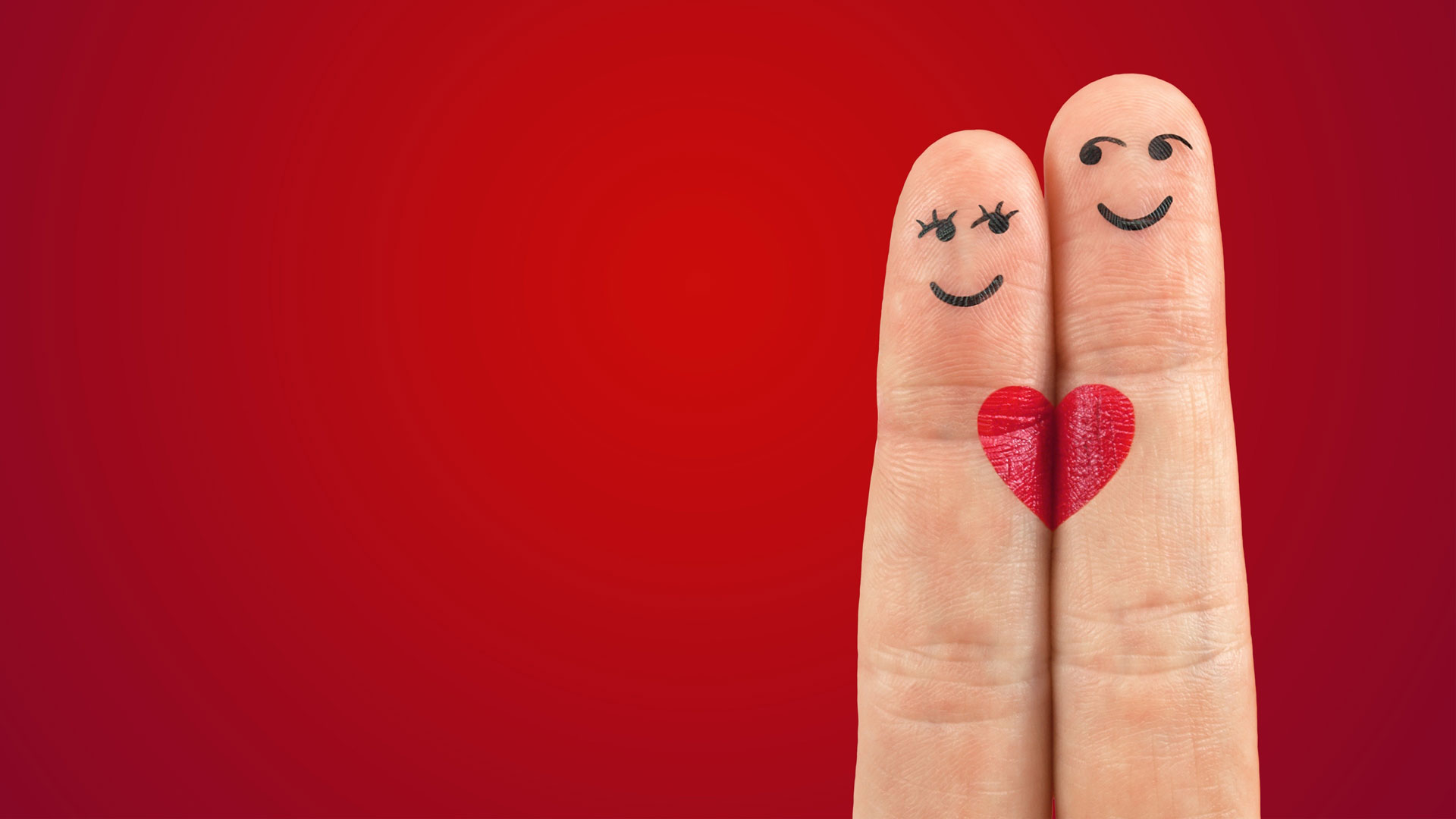 Zwei Finger mit je einem aufgemalten weiblichen und männlichen Gesicht sowie einem roten Herzen